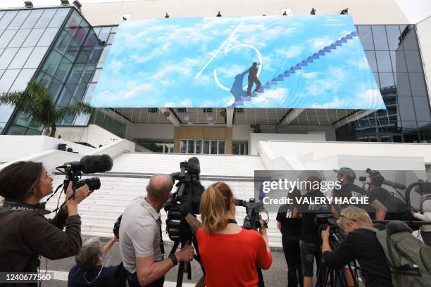 Photographers take pictures as workers set up the official poster of the 75th Cannes Film Festival on the facade of the Palais des Festivals, in...