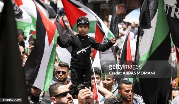 Palestinian wave national flags as they march in a rally marking the 74th anniversary of the "Nakba" or "catastrophe", in the occupied West Bank town...