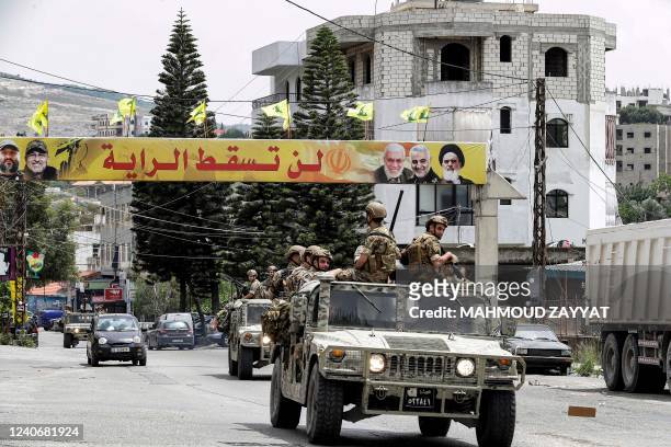 Lebanese army vehicles drive past a banner for the Lebanese Shiite Muslim movement Hezbollah with text in Arabic reading "the flag will not fall" and...