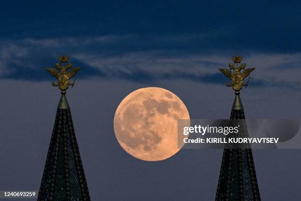 The full moon also known as Flower blood moon is pictured behind the two-headed eagle, the national symbol of Russia atop a building on Red Square in...