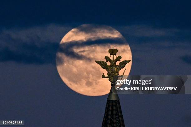 The full moon also known as Flower blood moon is pictured behind the two-headed eagle, the national symbol of Russia atop a building on Red Square in...