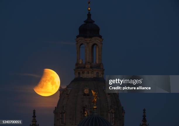 May 2022, Saxony, Dresden: The moon sets in the morning during a lunar eclipse behind the Frauenkirche and the dome of the Kunstakedmie with the...