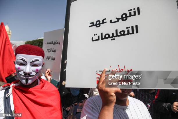 Protestor wearing Anonymous Mask, stands next to another protestor raising a placard that reads in Arabic, the era of instructions is over, during a...