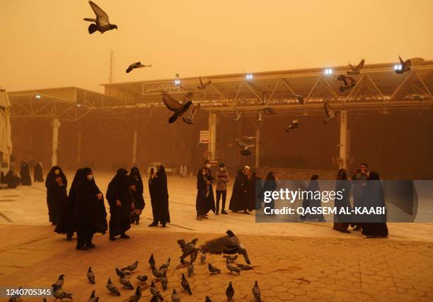 Visitors from Iran take pictures as they feed pigeons during a sandstorm in Iraq's holy city of Najaf on May 16, 2022. - Another sandstorm that...