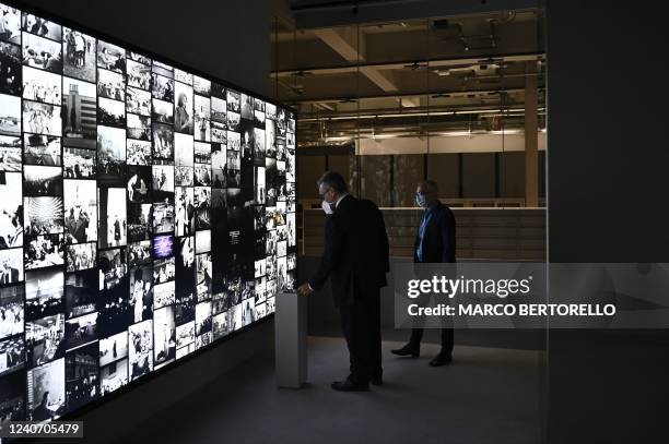 Two men stand in front of the screen with pictures from Intesa Sanpaolo Publifoto Archive at the Gallerie dItalia Torino in the northern city of...