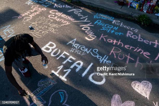 Aaron Jordan, of Buffalo, adds to a sidewalk chalk mural depicting the names of the people killed yesterday as people gather at the scene of a mass...