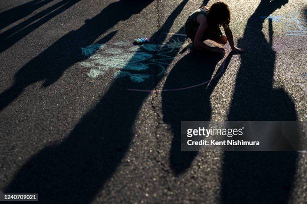 Child draws on the street with sidewalk chalk, as people gather at the scene of a mass shooting at Tops Friendly Market at Jefferson Avenue and Riley...