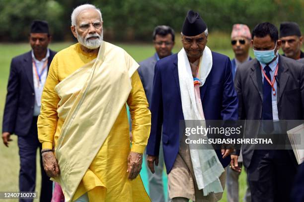 India's Prime Minister Narendra Modi walks along with his Nepali counterpart Sher Bahadur Deuba after offering prayers at the Mayadevi temple on the...