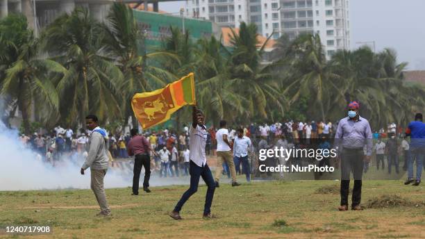 Sri Lankan pro-government protester runs with a Sri Lankan flag amid tear gas as they clash with anti-government protesters at Gotagogama near the...