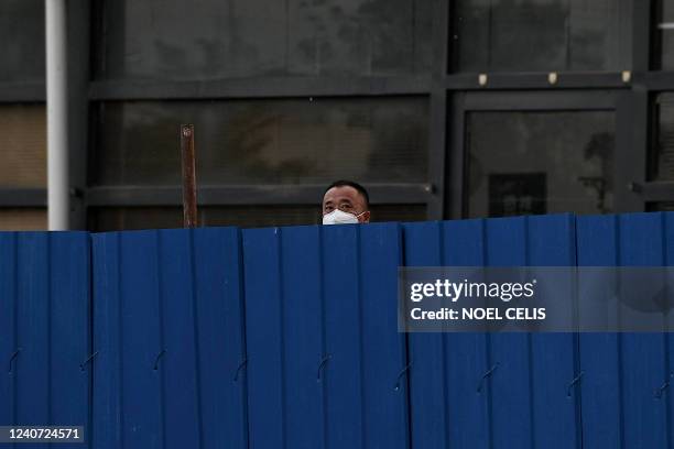 Man looks out while being confined inside a fenced residential area under lockdown due to Covid-19 coronavirus restrictions in Beijing on May 17,...