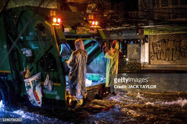 Waste disposal workers wear ponchos as they ride down a flooded street after heavy rain in Bangkok on May 18, 2022.