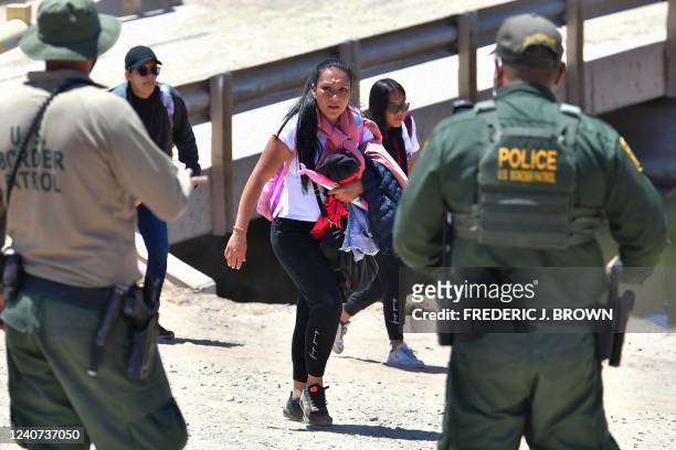 Customs and Border Protection officers look on as migrants on the Mexico side approach a gap in the border wall across from Yuma, Arizona on May 16,...