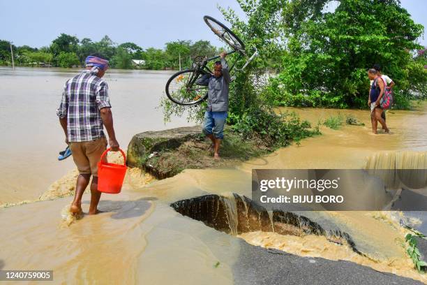 Man carrying his bicycle crosses a damaged road due to flooding after heavy rains in Nagaon, Assam, on May 19, 2022. - At least 10 people, including...