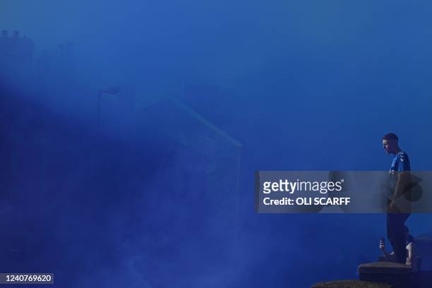 An Everton's supporter stands on a roof among blue smoke as fans arrive to attend the English Premier League football match between Everton and...