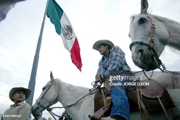 Farmer mounted on a horse confers with fellow demonstrators beneath the Mexican national flag 31 January 2003 in Mexico City 2003 to protest the...