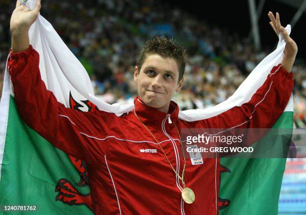 David Davies of Wales holds his country's flag following the awards ceremony for his victory in the men's 1500m freestyle final at the Commonwealth...