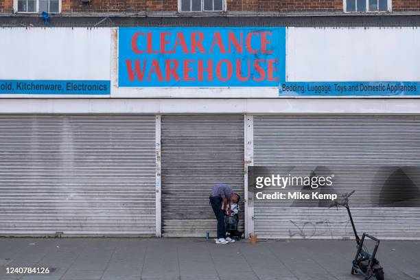 Man playing the accordian for money outside the closed down and shuttered clearance warehouse shop front at Turnpike Lane in Wood Green as the...