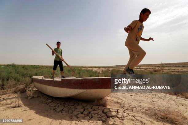 Boy holds an oar while another prepares to jumps off the prow a grounded boat on the dried up soil of what was Lake Hamrin in Iraq's Diyala province...