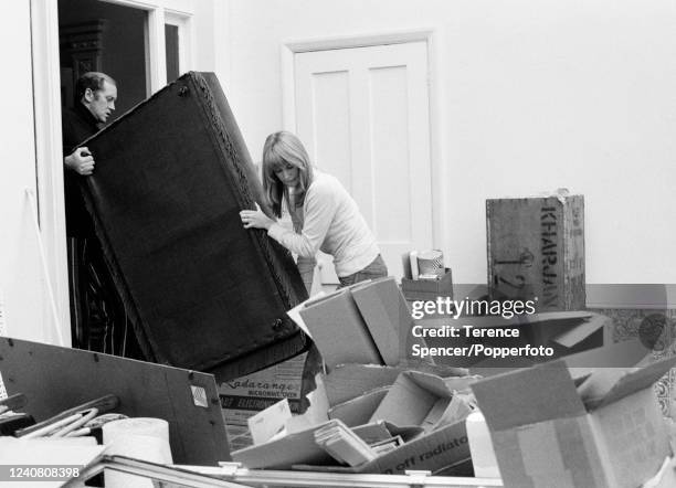 Husband and wife actors Jill Townsend and Nicol Williamson moving furniture amongst packing boxes in their conservatory at home in London, circa...