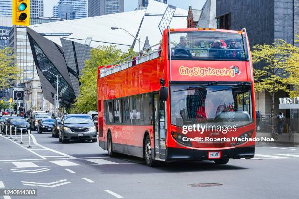 Double-decker tourist bus belonging to City Sightseeing company drives in Bloor St. The Royal Ontario Museum or ROM can be seen in the background.