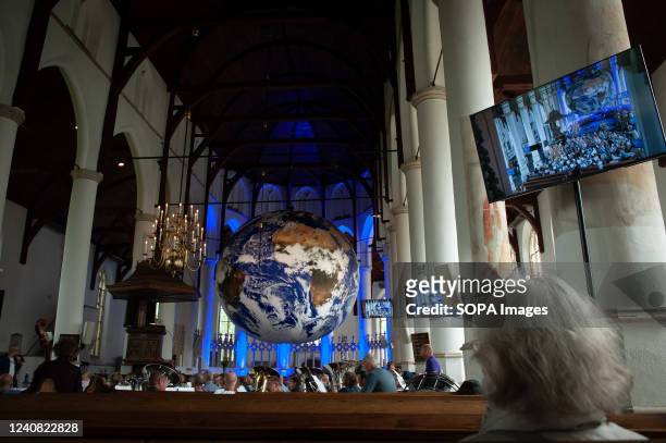 Woman is seen sitting in church while looking at a big Earth ball. Gaia is a touring artwork by UK artist Luke Jerram. Measuring seven meters in...