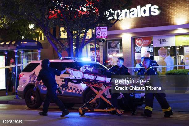 Paramedics transport a person who was wounded by gunfire at the scene where five people were shot near the intersection of East Chicago Avenue and...