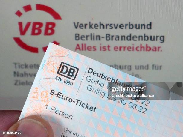 May 2022, Brandenburg, Potsdam: A man's hand holds a 9-euro ticket in front of the words "Verkehrsverbund Berlin-Brandenburg Alles ist erreichbar" on...