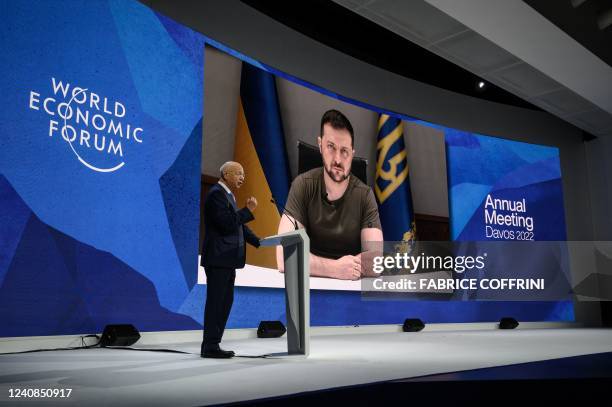 Founder and executive chairman of the World Economic Forum Klaus Schwab welcomes Ukrainian President Volodymyr Zelensky seen on a giant screen by...