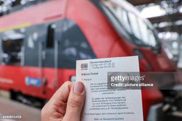 May 2022, Saxony, Leipzig: A woman stands with a 9-euro ticket in front of a regional express train of the Deutsche Bahn at the main station in...