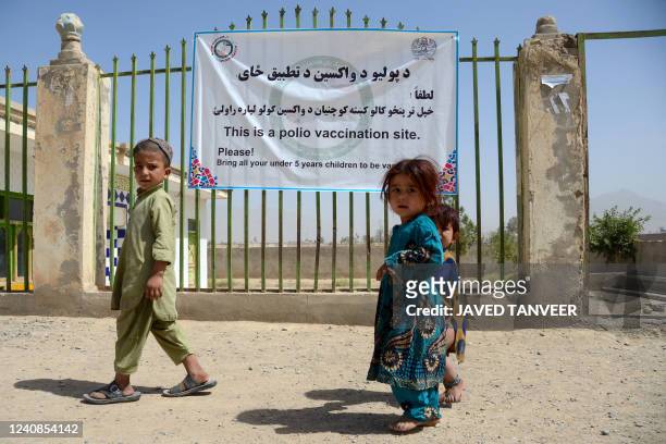 Children walk past a polio vaccination campaign banner in Kandahar on May 23, 2022.