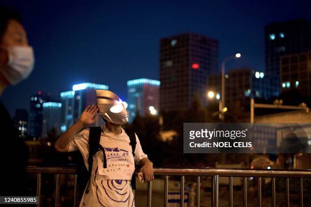 Man wearing an Ultraman mask stands along a bridge in Beijing on May 23, 2022.