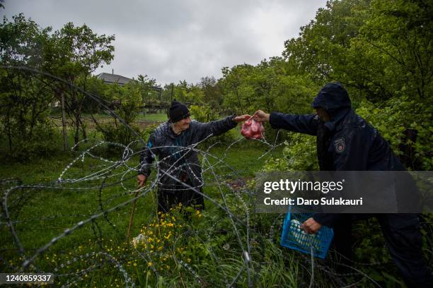 Georgian border police hand food over a barbed wire fence to local farmer, who stands on the Russian controlled territory of South Ossetia in...