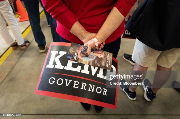 An attendee holds a campaign flyer and sign during a campaign event for Brian Kemp, governor of Georgia, in Kennesaw, Georgia, US, on Monday, May 23,...