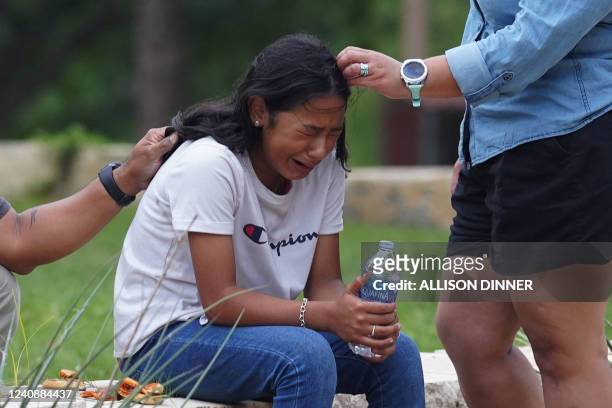 Girl cries, comforted by two adults, outside the Willie de Leon Civic Center where grief counseling will be offered in Uvalde, Texas, on May 24,...