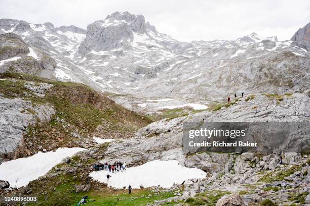 Surrounded by icy mountain peaks, a school tour group gather on a small patch of snow for a photo near the cablecar station at Fuente De in the...