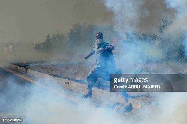 Supporter of Pakistan's former prime minister Imran Khan, runs amid tear gas fired by police during a protest rally in Swabi on May 25, 2022. - Khan...