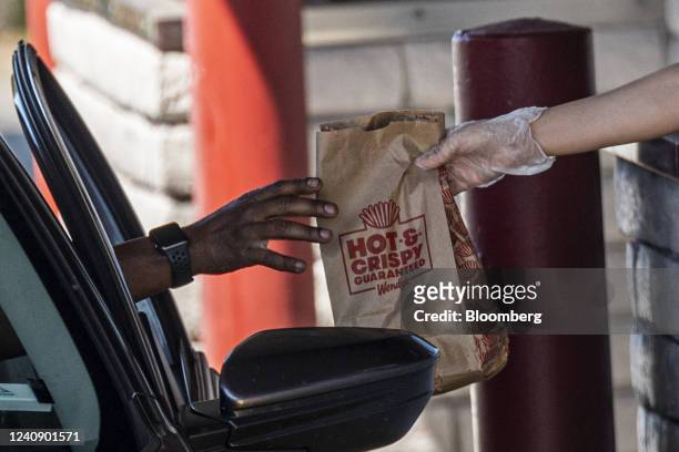 Worker hands a customer their order in the drive-through of a Wendy's fast food restaurant in Pinole, California, US, on Wednesday, May 25, 2022....