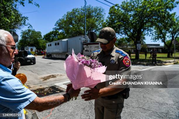 Police officer takes flowers from a resident to be placed at a makeshift memorial outside Robb Elementary School in Uvalde, Texas, on May 25, 2022. -...