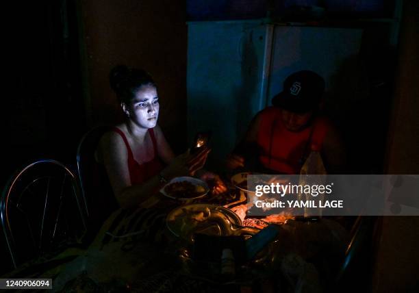 Woman looks at her cell phone while eating next to a man by the light of a candle during a blackout in Havana, on May 25, 2022. - The main...