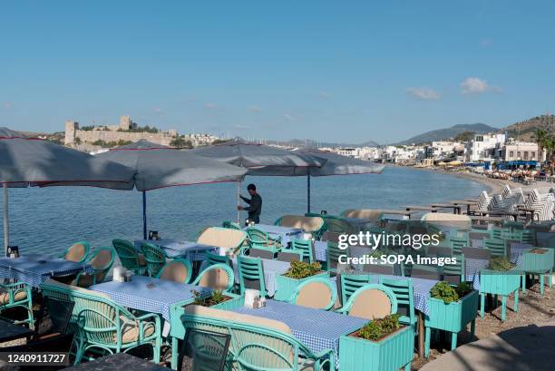 Waiter prepares tables on the beachside cafe in Bodrum harbor with Bodrum Castle in the background, the Aegean coast of southwest Turkey.