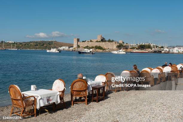 Restaurant Tables on the beach in Bodrum harbour with Bodrum Castle in the background, the Aegean coast of south west Turkey.