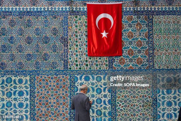 Man prays in front of beautiful Iznik tiles with a Turkish flag seen outside the tomb of Abu Ayyub al-Ansari in the Eyup Sultan mosque on the banks...
