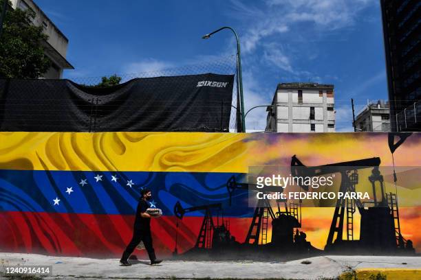 Man wearing a face masks walks past a mural depicting an oil pump and the Venezuelan flag in a street of Caracas, on May 26, 2022.