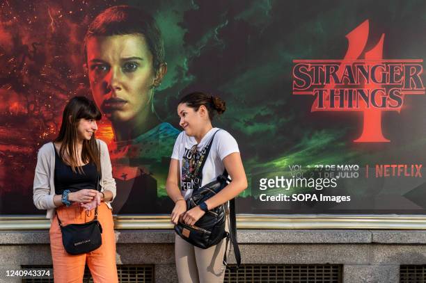 Women talk in front of a street commercial advertisement banner from the American global on-demand Internet streaming media provider Netflix...