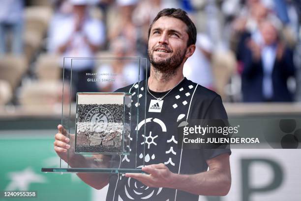 France's Gilles Simon poses with a trophy he received to mark his last participation in the Roland-Garros Open tennis tournament after losing his...