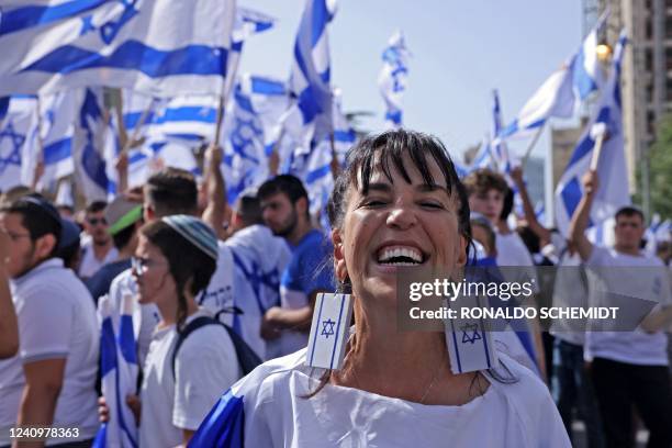 Woman wearing earrings depicting the Israeli flag smiles before demonstrators chanting slogans and waving Israeli flags in Jerusalem on May 29 ahead...