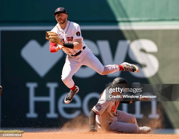 Trevor Story of the Boston Red Sox leaps over Adley Rutschman of the Baltimore Orioles after turning a double play to end during the fourth inning at...