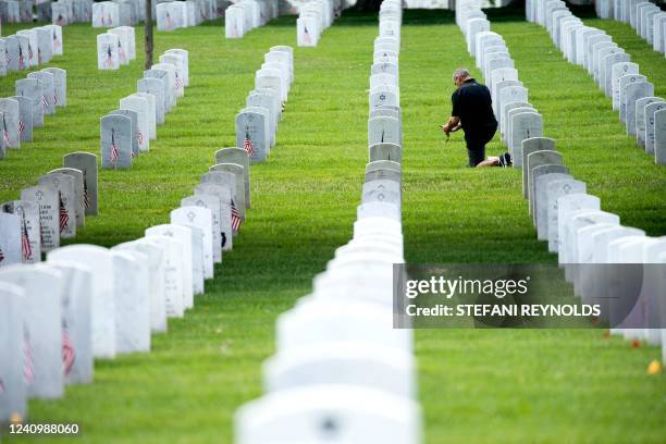 Man kneels in front of a grave near Section 60 at Arlington Cemetery in Arlington, Virginia, on May 29, 2022.