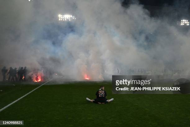 Football fan sits on the pitch as riot police officers in background clash with Saint-Etienne's fans who invaded the pitch after being defeated by...
