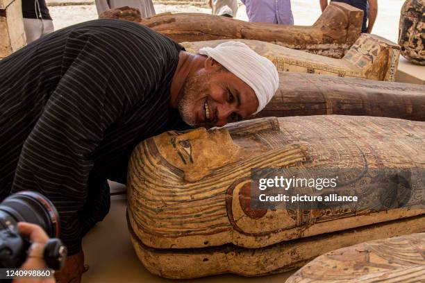 May 2022, Egypt, Saqqara: A member of the excavation team poses next to a wooden sarcophagus at a media opportunity during which a new archaeological...